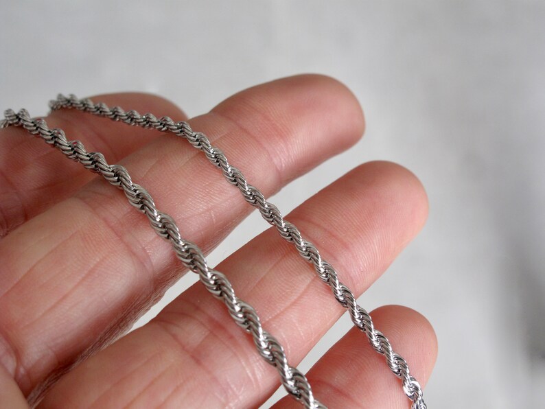May include: Two silver rope chains of different thicknesses, laid out on a hand.