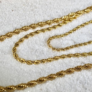 May include: Two gold rope chains of different lengths, lying on a white surface.