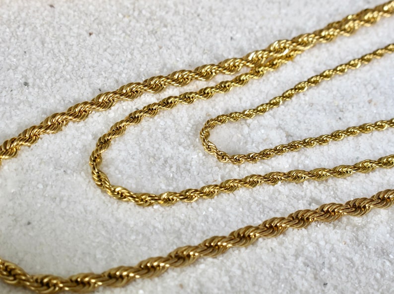 May include: Two gold rope chains of different lengths, lying on a white surface.