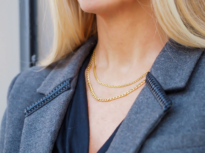May include: A woman wearing a gray jacket with a black shirt underneath. She is wearing two gold chain necklaces.