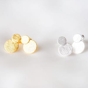 Peut inclure: Une paire de boucles d'oreilles avec trois disques ronds texturés. Une boucle d'oreille est dorée et l'autre est argentée.