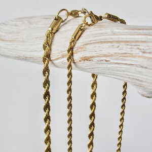 May include: Three gold-toned rope chains of varying lengths, displayed on a white wooden surface.