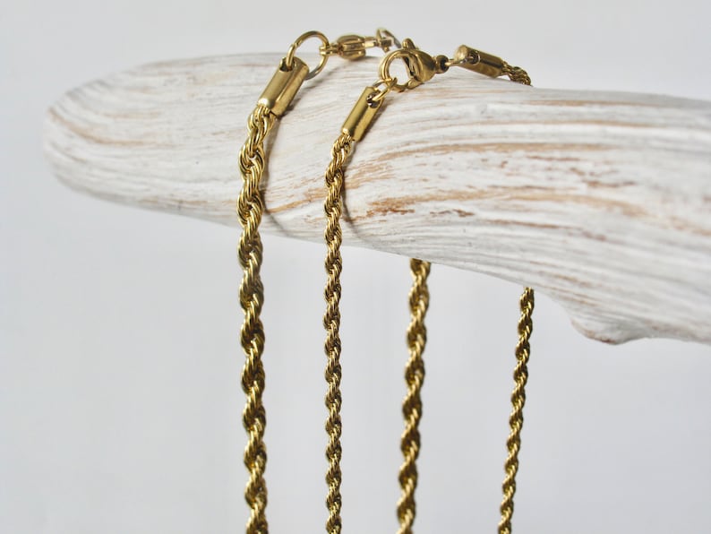May include: Three gold-toned rope chains of varying lengths, displayed on a white wooden surface.