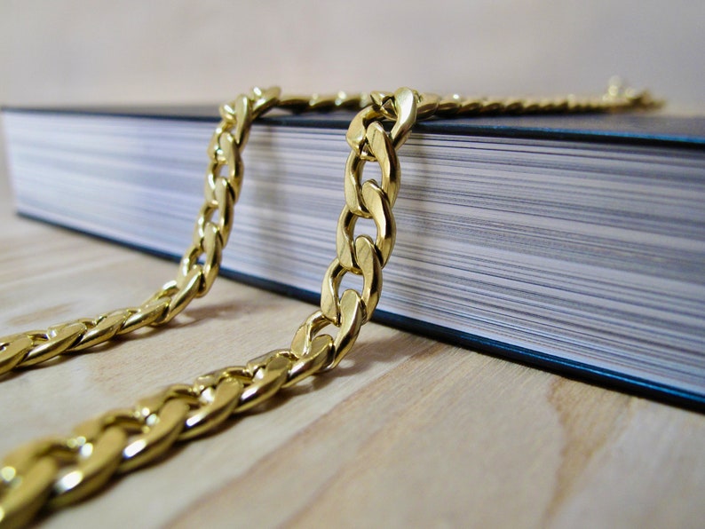 May include: A gold chain necklace on a black book. The chain is thick and has a curb link design.