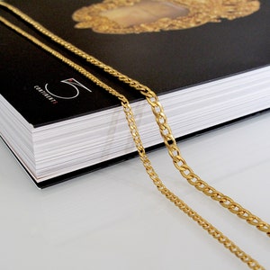 May include: Two gold chains, one thicker than the other, are draped over a black book with the word "CONTINENTS" printed on the cover.