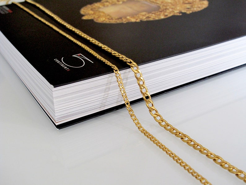 May include: Two gold chains, one thicker than the other, are draped over a black book with the word "CONTINENTS" printed on the cover.