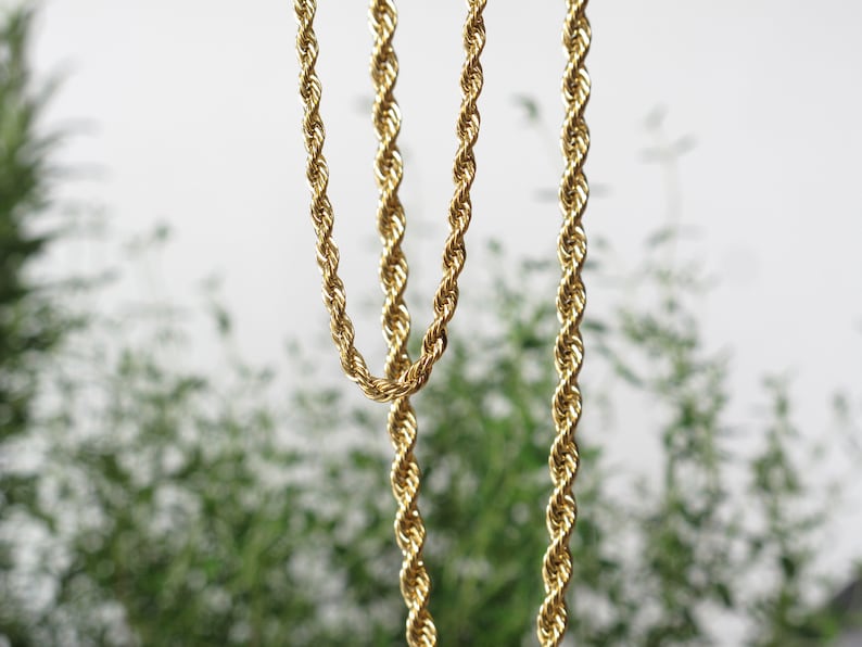 May include: Two gold rope chains hanging against a blurred green background.