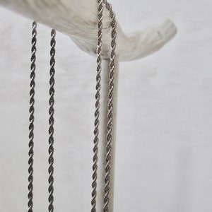 May include: Three silver rope chains hanging from a wooden branch. The chains are all the same length and thickness.