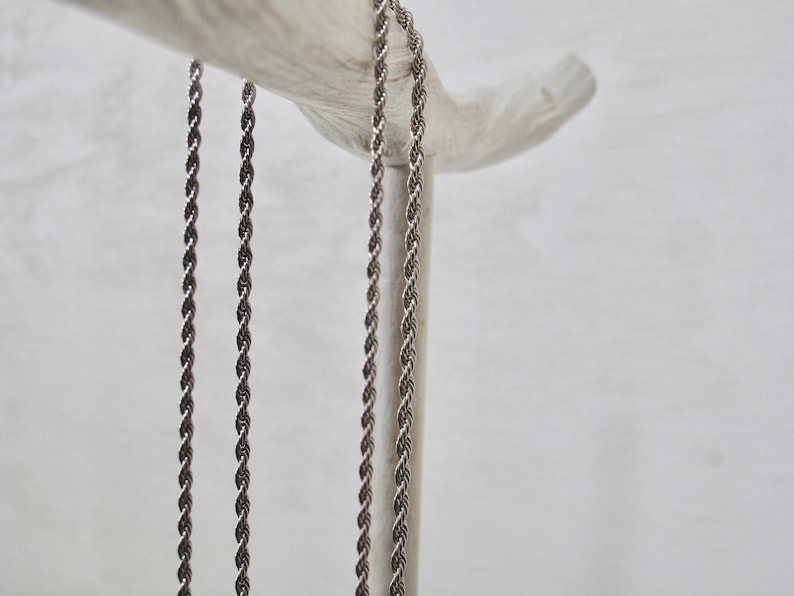 May include: Three silver rope chains hanging from a wooden branch. The chains are all the same length and thickness.