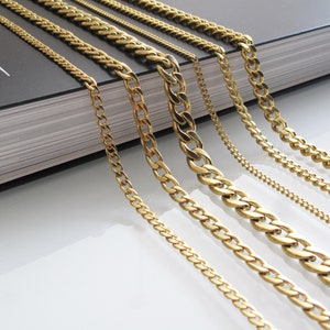 May include: A set of seven gold chains of varying widths and lengths. The chains are arranged in a fan shape on a black book with the word "CONTINENT" printed on the cover.