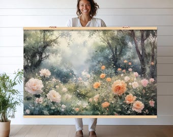 Op de afbeelding: Een ingelijste bloemenprint met een aquarel van een rozentuin. Het kunstwerk toont perzik- en roze rozen, weelderig groen en hoge bomen. De print wordt vastgehouden door een persoon in een wit overhemd en een witte broek.