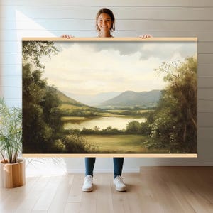 Op de afbeelding: Een schilderij van een landschap met een meer op de voorgrond, omringd door groene heuvels en bomen. De lucht is lichtblauw met witte wolken.