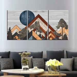 May include: A three-panel wall art set featuring a mountain landscape design. The artwork showcases geometric mountain shapes in shades of brown, orange, and gray, with a blue circle representing the moon. Trees are also included in the design, set against a light gray wood-grain background.