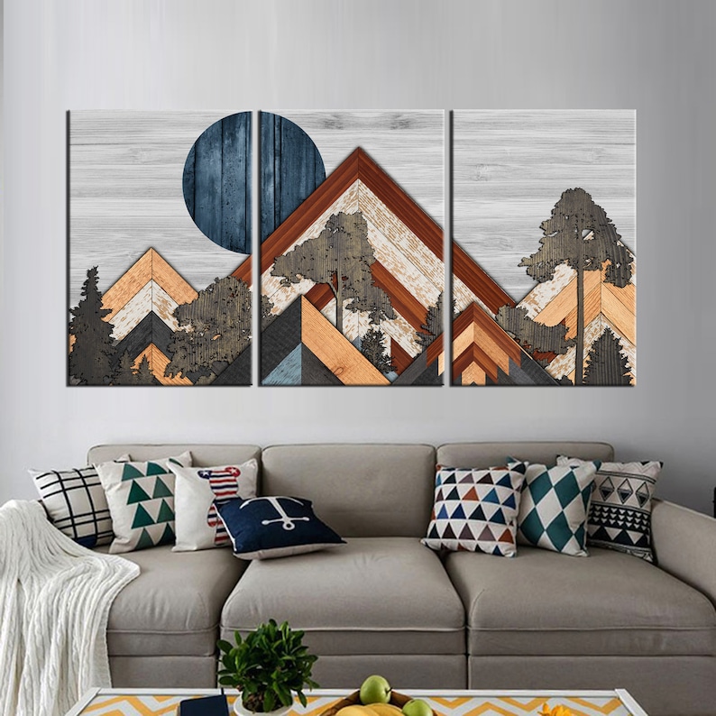 May include: A three-panel wooden wall art piece depicting a mountain landscape with a blue moon. The artwork features layered wood in shades of brown, orange, gray, and blue, with tree silhouettes. The background is a light gray wood grain.