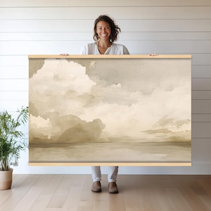 Op de afbeelding: Een ingelijst aquarel schilderij van een zeegezicht in een lichtbruin en beige kleurenschema. Het schilderij toont een bewolkte lucht boven een kalme watermassa.