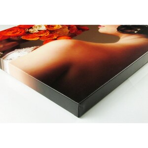 May include: A close-up of a canvas print featuring a bride holding a bouquet of orange and white flowers. The print is mounted on a black frame.