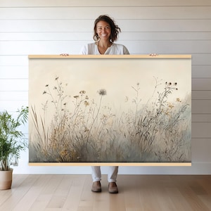 Puede incluir: Una gran impresión de arte mural rectangular con una pintura de acuarela de un campo de hierbas altas y flores silvestres en tonos apagados de beige, gris y marrón. La obra de arte está sujeta por un marco de madera.