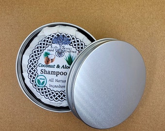 Op de afbeelding: Een zilveren blik met een wit etiket waarop staat "Folks Soap Hand Crafted Coconut & Aloe Shampoo All Natural Ingredients Vegan". Het blik is open en het deksel ligt ernaast.