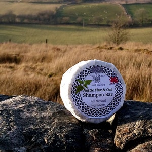 May include: A white round bar of soap with a black and white Celtic knot design. The label reads "Folk Soap Hand Crafted Nettle Flax & Oat Shampoo Bar All Natural Ingredients".
