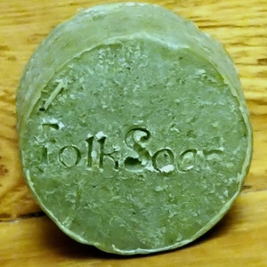 May include: A round, green bar of soap with the word "Folk Soap" embossed on the top.