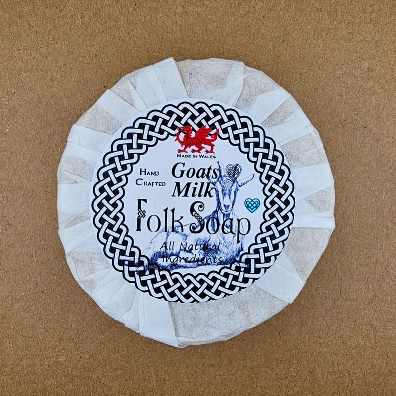 May include: A white round bar of goat milk soap with a black and white label that says "Hand Crafted Goats Milk Folk Soap" with a red dragon and a goat illustration. The label also says "Made in Wales" and "All Natural Ingredients".