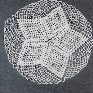 Puede incluir: Doily de ganchillo blanco con un diseño en forma de estrella en el centro.