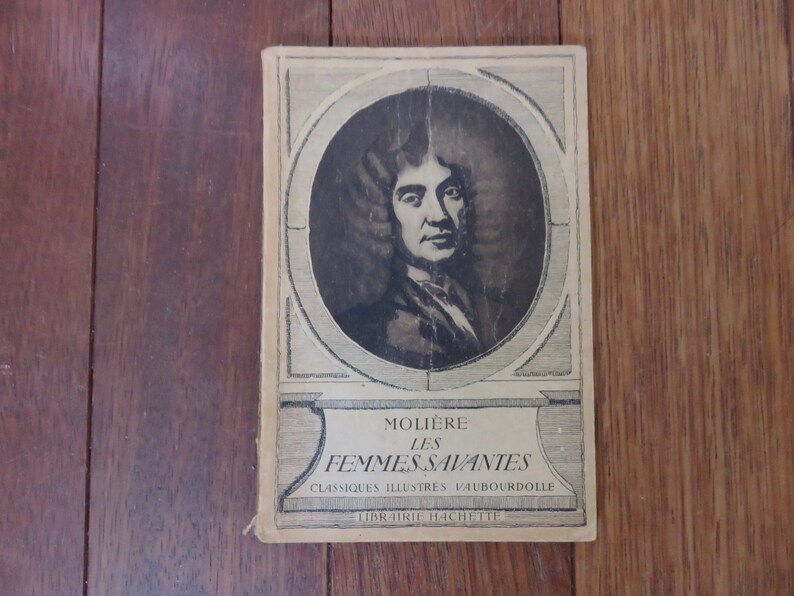 May include: A vintage book cover featuring a black and white portrait of Moli&egrave;re, the French playwright. The title of the book is "Moli&egrave;re Les Femmes Savantes" with the words "Classiques Illustres V.AUBOURDOILLE" and "Librairie Hachette" printed below.