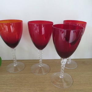 Può includere: Set di quattro bicchieri da vino rosso con steli intrecciati. I bicchieri sono trasparenti e hanno una tonalità rossa.