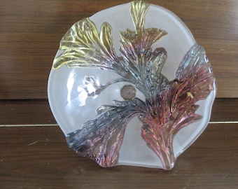 Può includere: Un piatto da portata in vetro trasparente con un design a rilievo di fiori iridescenti in tonalità di giallo, blu e rosa.