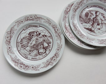 Op de afbeelding: Set van vier witte keramische borden met een bruine bloemenrand en illustraties van vrouwen in traditionele Franse kleding. De borden tonen de tekst "La Lavandiere" en "La Marchande de Lait".