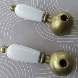 May include: Two antique white porcelain and brass faucet handles. The handles are shaped like a teardrop with a round brass base.