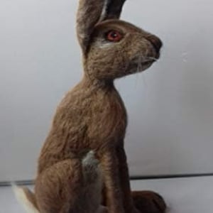 Könnte beinhalten: Handgefertigte braune Hasenfigur mit aufrechten Ohren und detaillierter Fellstruktur. Der Hase hat orangefarbene Augen und einen weißen Schwanz. Die Figur sitzt und zeigt ihre Vorderpfoten und ihre Gesamtform. Ein dekorativer Artikel.