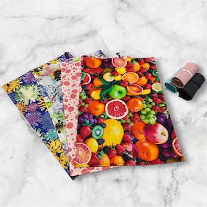 May include: A selection of patterned kitchen towels. One towel showcases a colourful fruit arrangement, while others feature floral and polka dot designs. Rolled towels in pink, teal, brown, and black are also present.