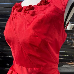 Puede incluir: Un vestido rojo sin mangas con un corpi&ntilde;o ajustado y una falda completa. El escote est&aacute; adornado con cinco grandes rosas de tela roja.