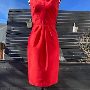 Puede incluir: Un vestido rojo sin mangas con un escote de volantes. El vestido es entallado y tiene una falda recta.