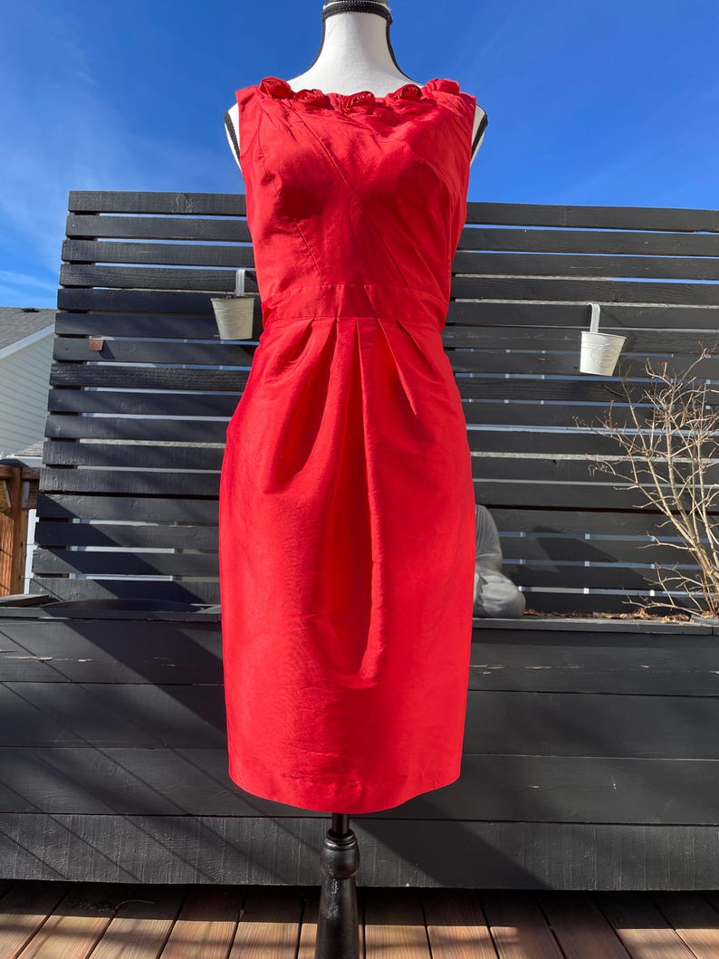 Puede incluir: Un vestido rojo sin mangas con un escote de volantes. El vestido es entallado y tiene una falda recta.