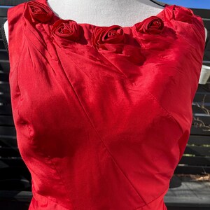 Puede incluir: Un vestido rojo sin mangas con escote redondo y una fila de rosas de tela roja en la parte superior.