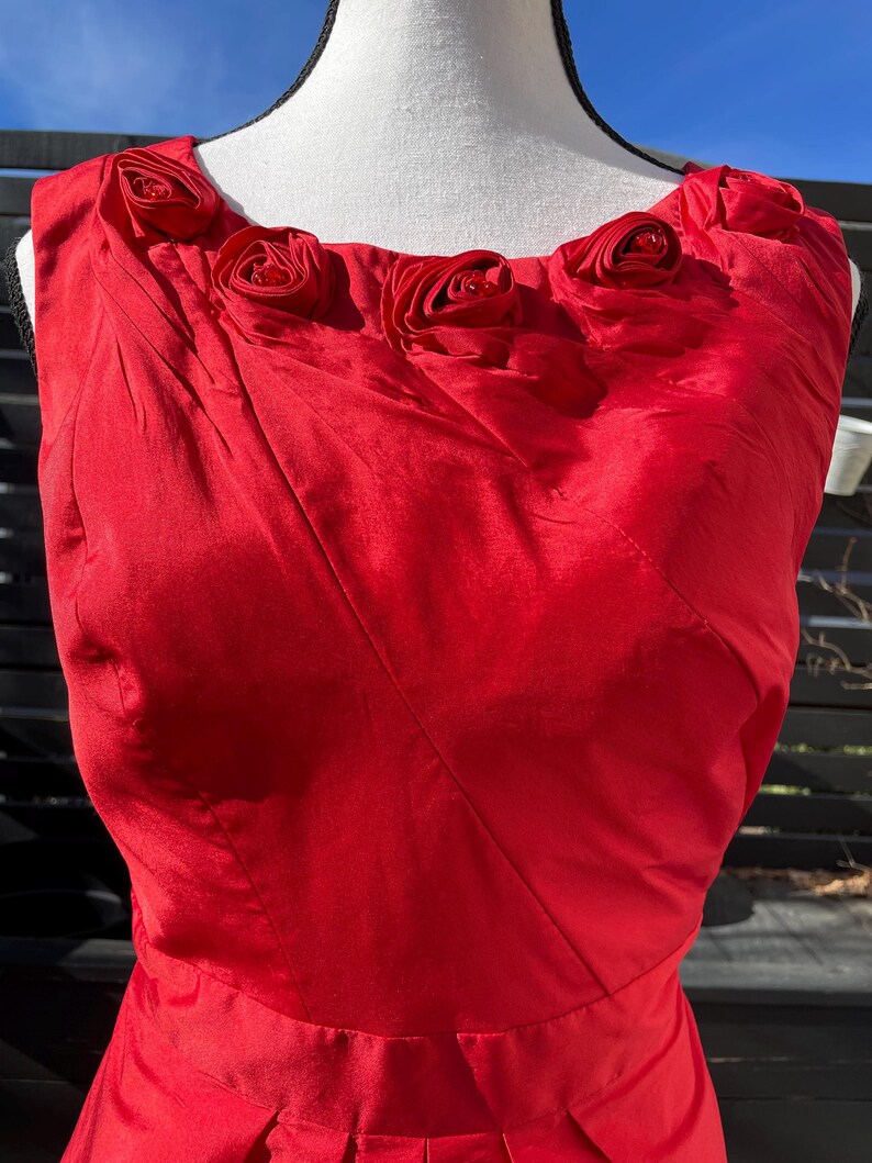 Puede incluir: Un vestido rojo sin mangas con escote redondo y una fila de rosas de tela roja en la parte superior.