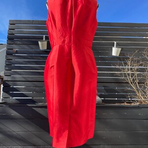 Puede incluir: Un vestido rojo sin mangas con un dise&ntilde;o sencillo. El vestido est&aacute; en un maniqu&iacute; y se fotograf&iacute;a contra una valla negra de listones.
