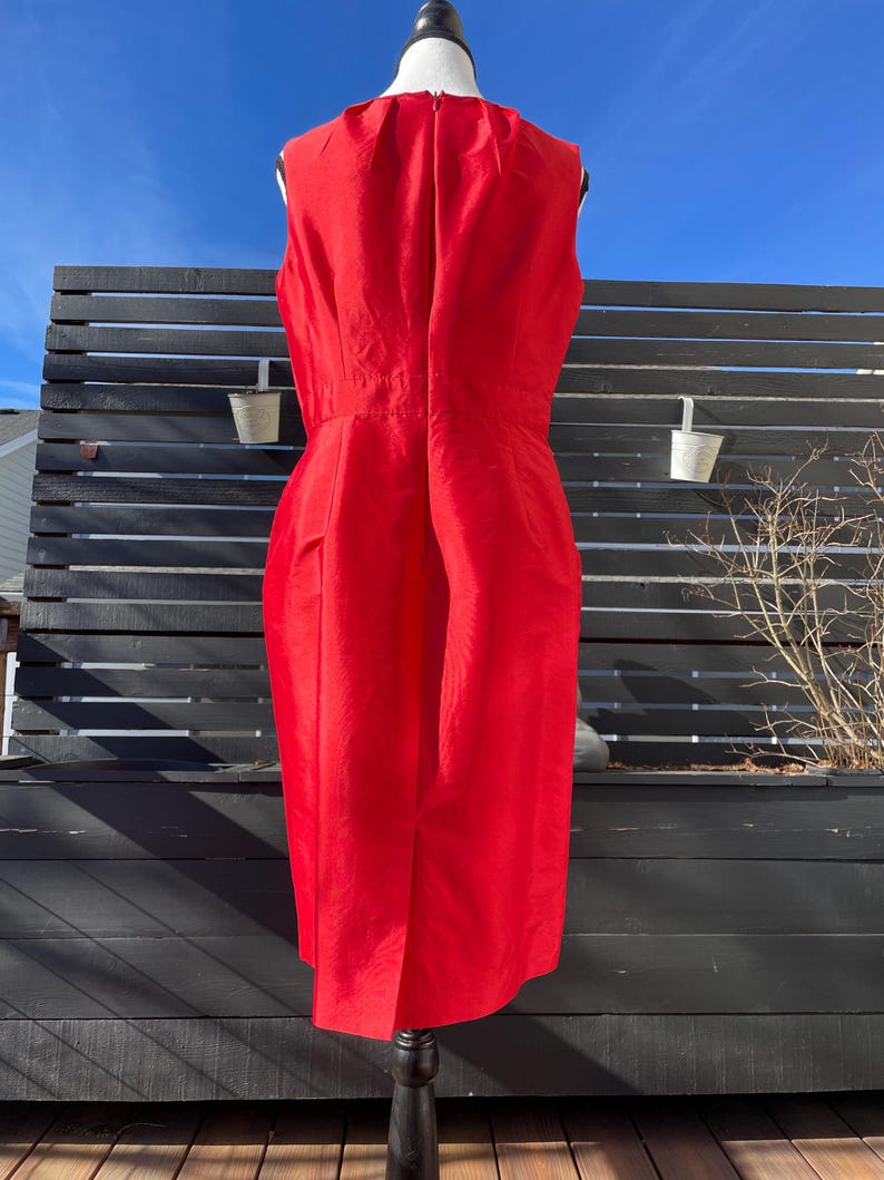 Puede incluir: Un vestido rojo sin mangas con un dise&ntilde;o sencillo. El vestido est&aacute; en un maniqu&iacute; y se fotograf&iacute;a contra una valla negra de listones.
