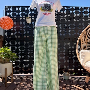 Puede incluir: Una camiseta blanca con un gráfico de oso y el texto "Yellowstone National Park Jackson Hole Wyoming", combinada con pantalones a cuadros verdes y blancos. El conjunto se exhibe en un maniquí.
