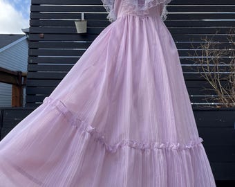 May include: A long, flowing lavender dress with a white lace bodice and ruffled sleeves. The dress has a tiered skirt and is made of a sheer fabric.