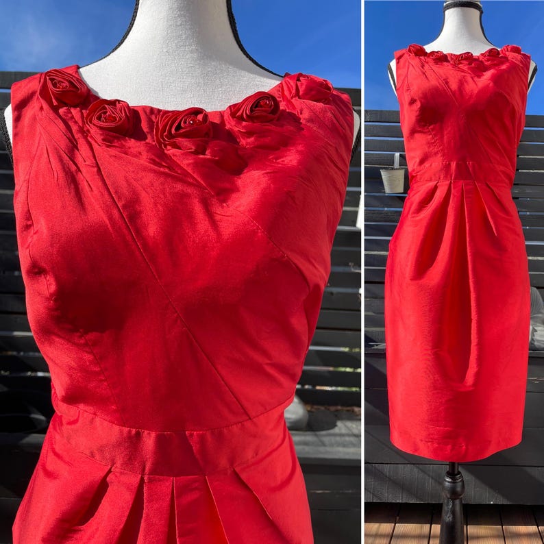 Puede incluir: Un vestido rojo sin mangas con un corpi&ntilde;o ajustado y una falda con pliegues. El vestido tiene un escote adornado con rosas de tela.