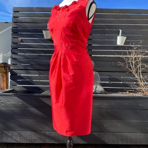 Puede incluir: Un vestido rojo sin mangas con un escote de volantes. El vestido es entallado y tiene una falda recta.