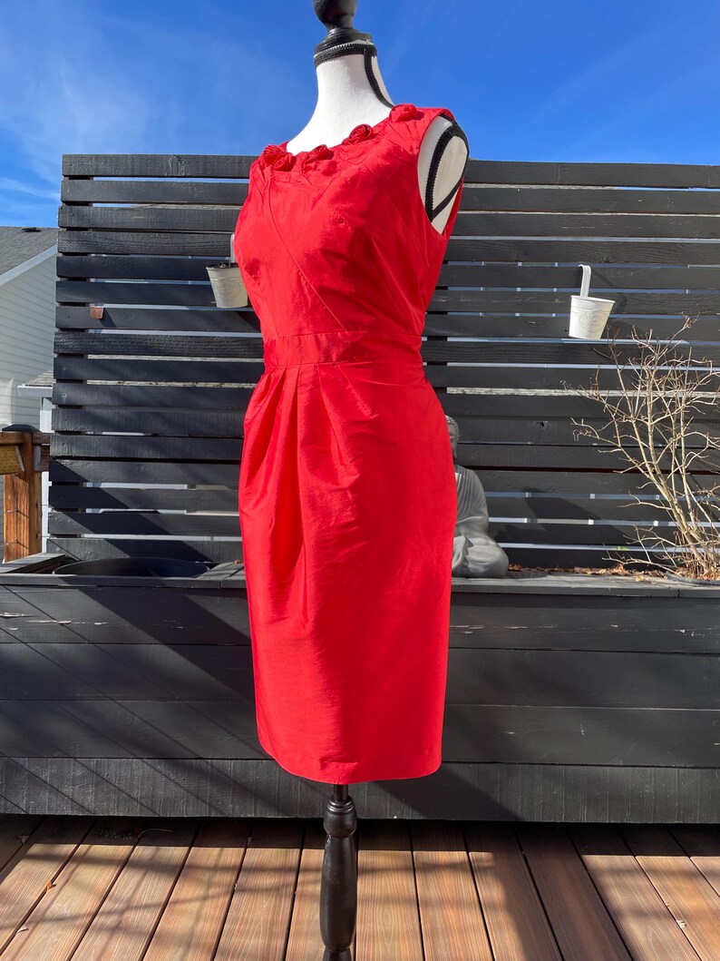Puede incluir: Un vestido rojo sin mangas con un escote de volantes. El vestido es entallado y tiene una falda recta.