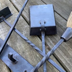 May include: A set of black metal fireplace tools with a twisted handle, a square shovel, and a broom with a black metal handle and natural bristles.