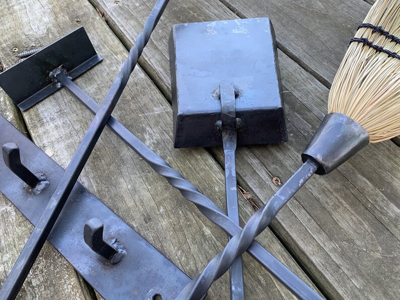 May include: A set of black metal fireplace tools with a twisted handle, a square shovel, and a broom with a black metal handle and natural bristles.