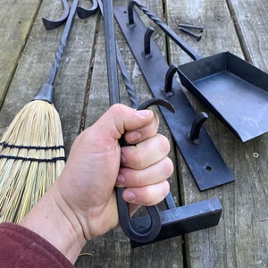 May include: A set of black metal fireplace tools with a brush, poker, shovel, and a wall-mounted rack with hooks. The tools are made of wrought iron and have a rustic finish.