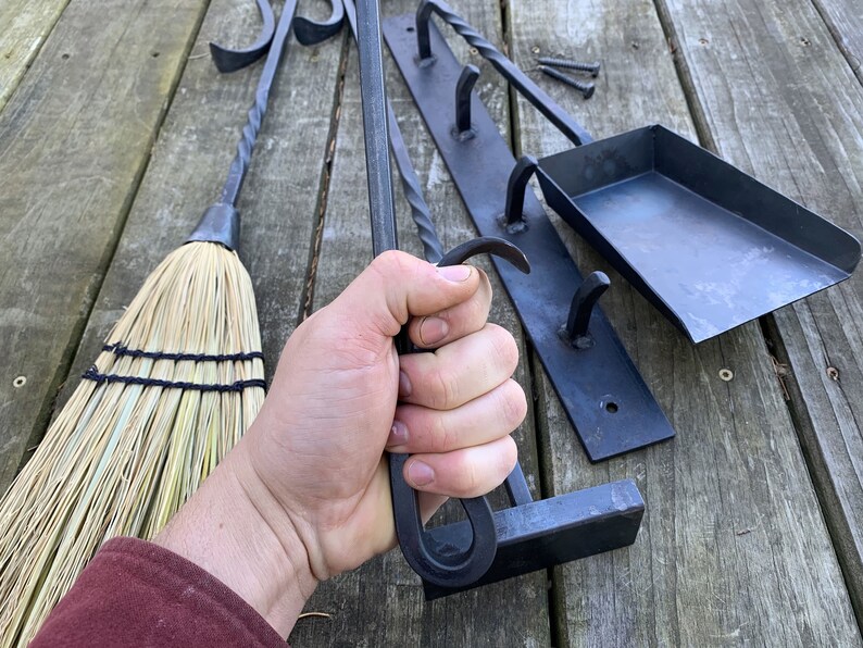 May include: A set of black metal fireplace tools with a brush, poker, shovel, and a wall-mounted rack with hooks. The tools are made of wrought iron and have a rustic finish.