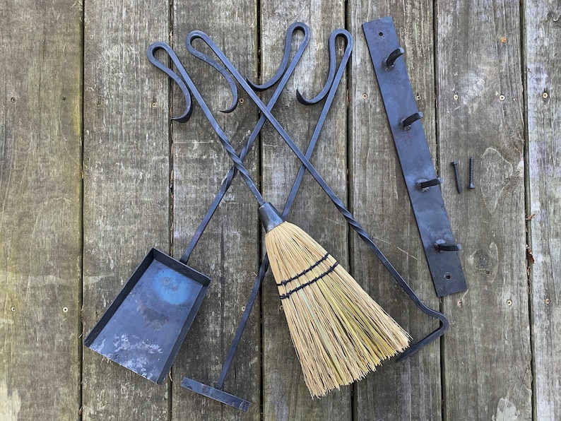 May include: A set of black metal fireplace tools with a matching wall-mounted rack. The tools include a poker, tongs, and a shovel. A natural fiber broom is also included.